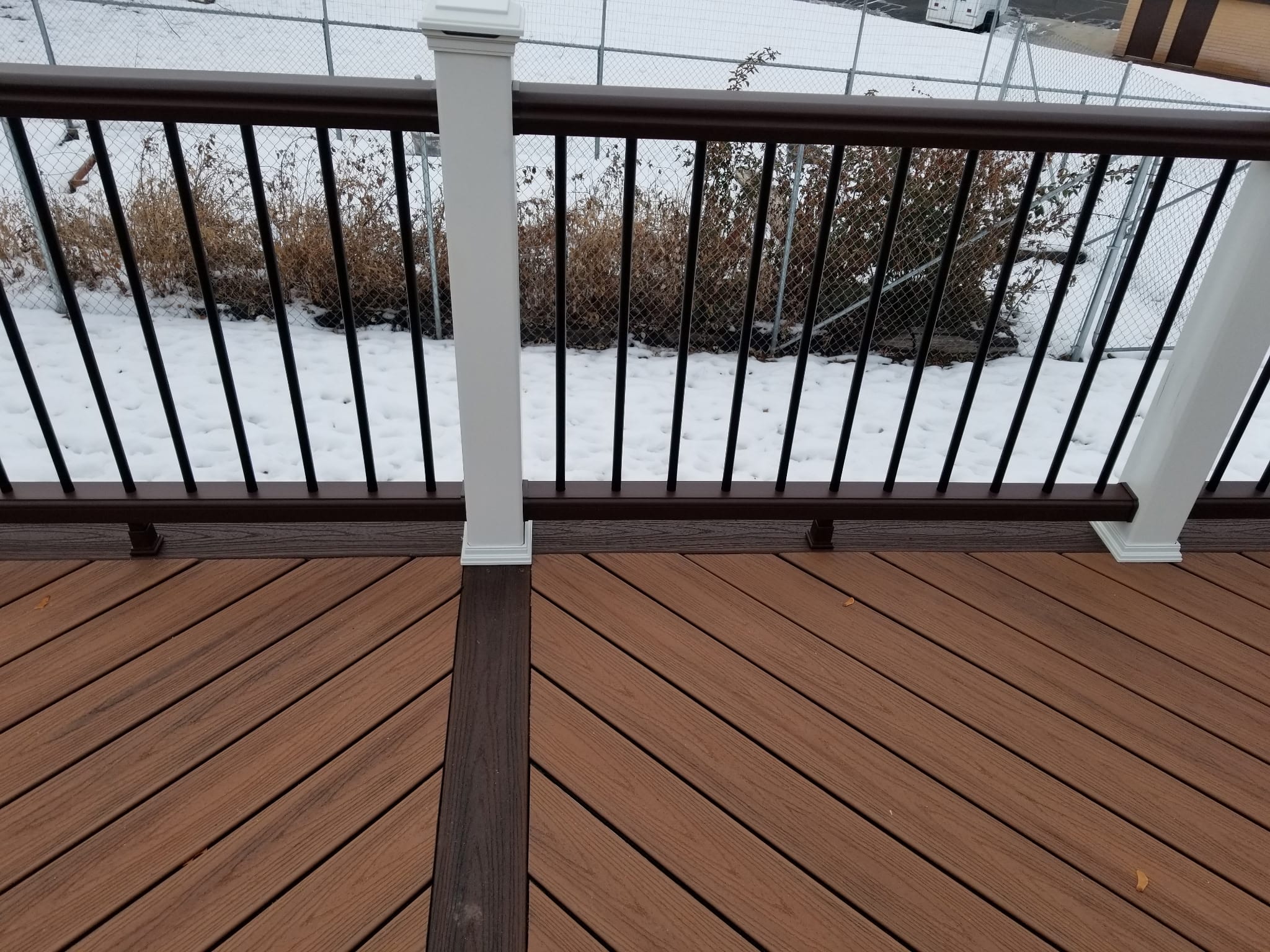 Wood-toned deck boards with a contrasting border, dark railing balusters, and white posts